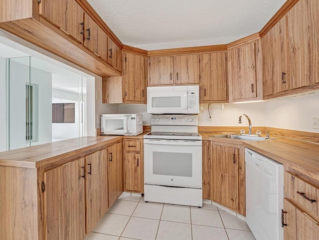 kitchen with light tile patterned floors, light countertops, a sink, white appliances, and a peninsula