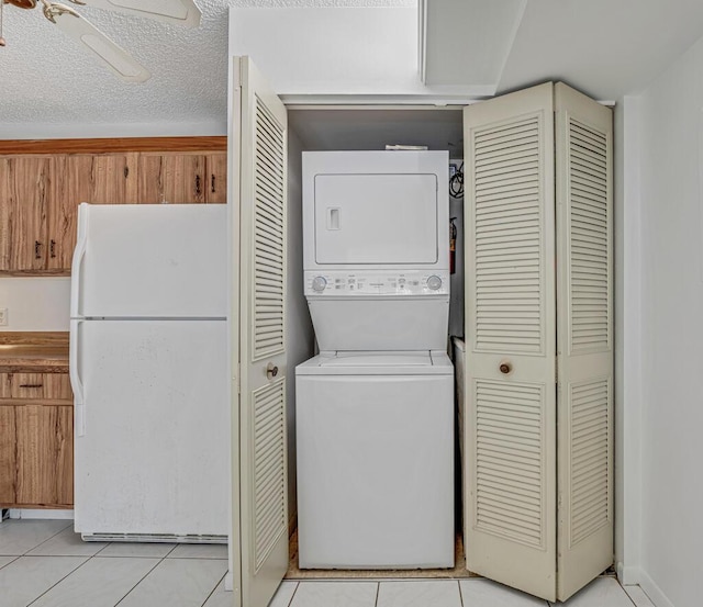 laundry room with laundry area, light tile patterned floors, a ceiling fan, stacked washer / drying machine, and a textured ceiling