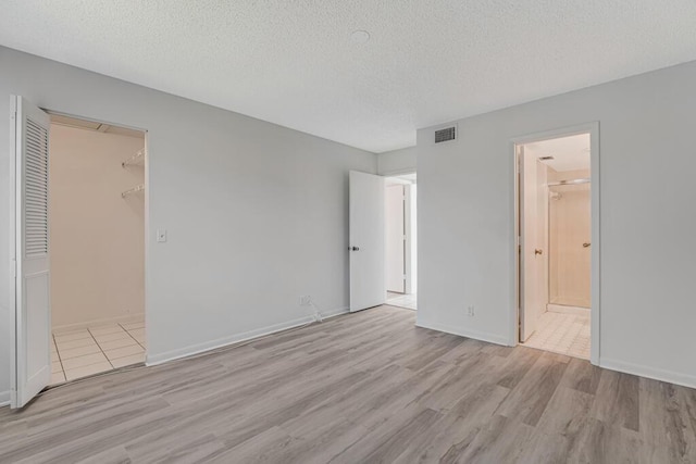 unfurnished bedroom with a textured ceiling, wood finished floors, visible vents, and connected bathroom