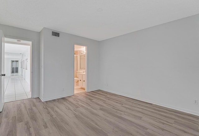 unfurnished bedroom with connected bathroom, wood finished floors, visible vents, and baseboards