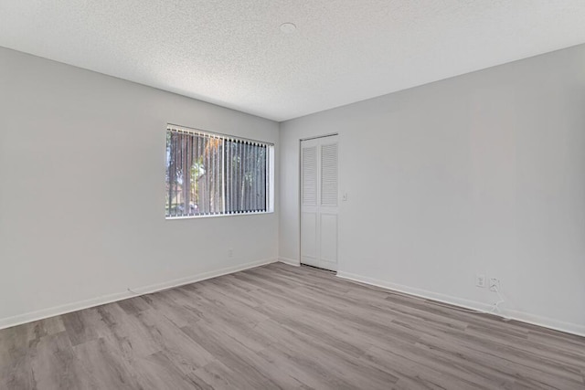 spare room featuring a textured ceiling, wood finished floors, and baseboards