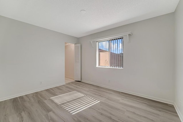 empty room with a textured ceiling, baseboards, and wood finished floors