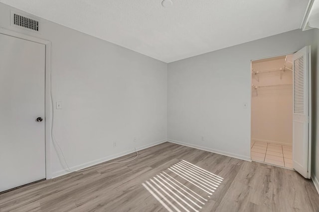 unfurnished bedroom featuring baseboards, visible vents, wood finished floors, a walk in closet, and a closet