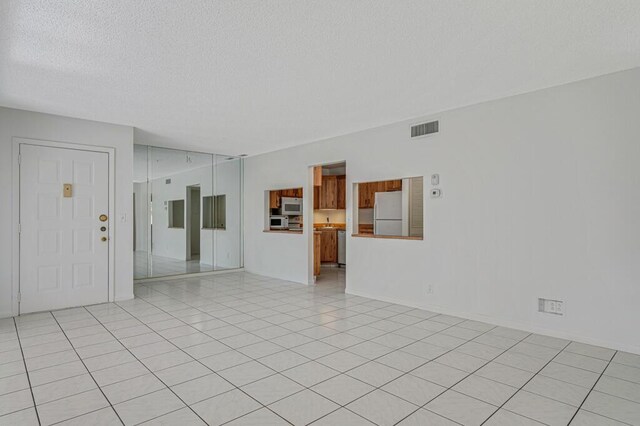 empty room with visible vents, a textured ceiling, and light tile patterned flooring