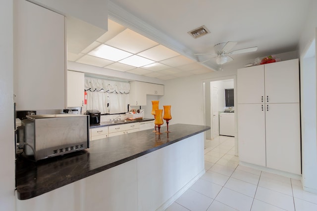 kitchen featuring washer / dryer, light tile patterned floors, visible vents, dark countertops, and a peninsula