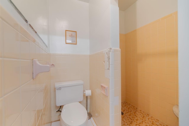 bathroom featuring toilet, a wainscoted wall, a tile shower, and tile walls