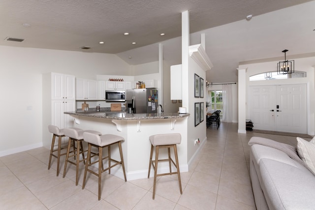 kitchen featuring visible vents, dark stone counters, appliances with stainless steel finishes, a breakfast bar, and vaulted ceiling