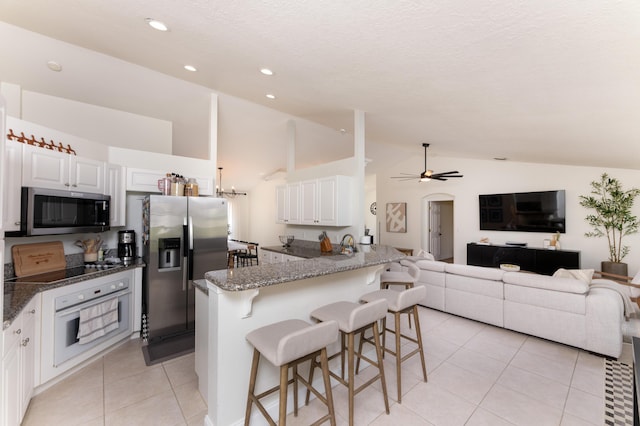 kitchen with stainless steel appliances, white cabinets, light tile patterned flooring, ceiling fan, and a kitchen bar