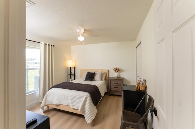 bedroom with light wood-style floors, ceiling fan, and a textured ceiling