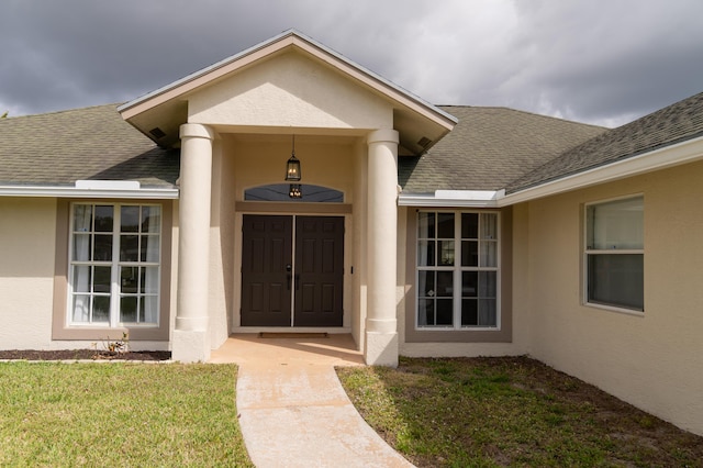 property entrance featuring roof with shingles, a yard, and stucco siding