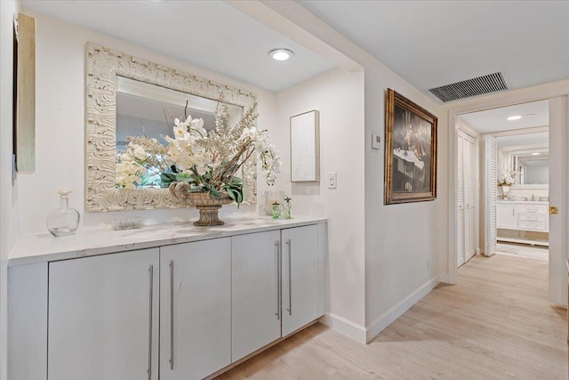 hall featuring a sink, light wood-style floors, visible vents, and baseboards