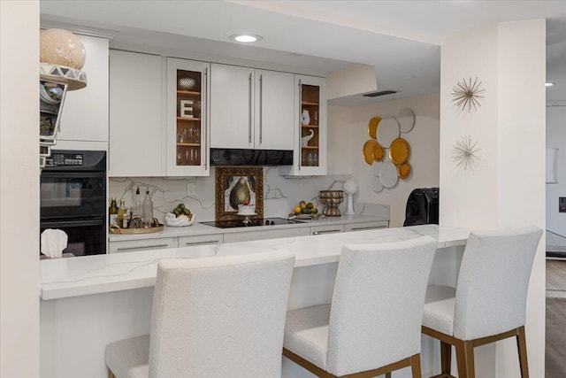 bar featuring decorative backsplash, black appliances, visible vents, and under cabinet range hood