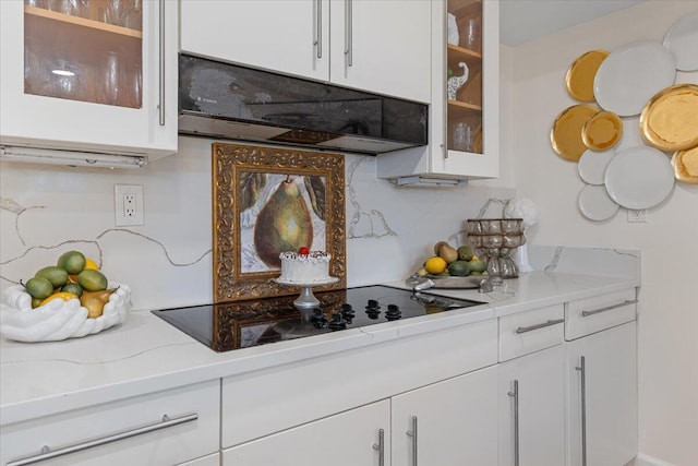 kitchen with glass insert cabinets, tasteful backsplash, range hood, white cabinets, and black electric cooktop