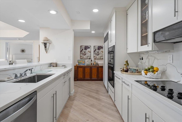 kitchen featuring a sink, light stone counters, stainless steel dishwasher, light wood finished floors, and black electric stovetop