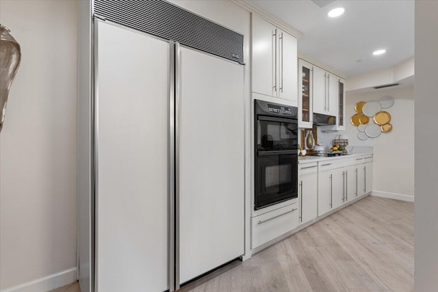 kitchen with baseboards, black appliances, light countertops, under cabinet range hood, and light wood-type flooring