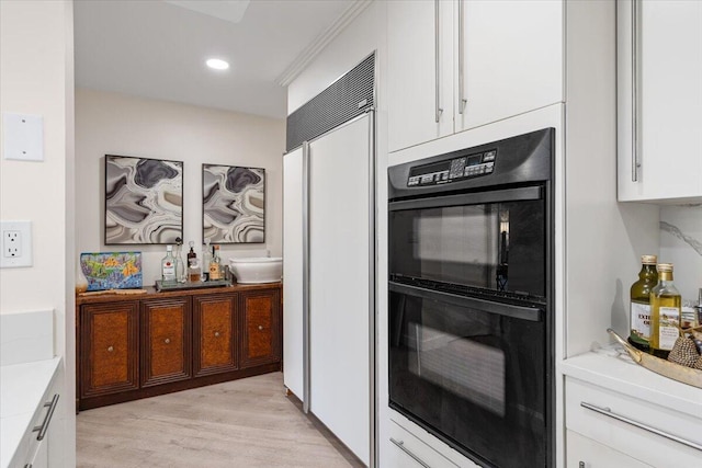 kitchen with light countertops, white cabinets, built in refrigerator, and dobule oven black