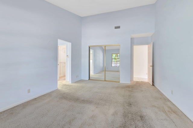 unfurnished bedroom with visible vents, light carpet, ensuite bath, a closet, and a towering ceiling