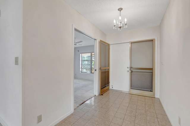 hall with a notable chandelier, light colored carpet, baseboards, and a textured ceiling