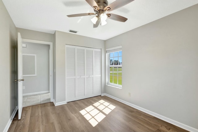 unfurnished bedroom with ceiling fan, wood finished floors, a closet, and baseboards