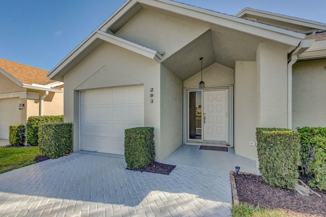 property entrance featuring decorative driveway, a garage, and stucco siding