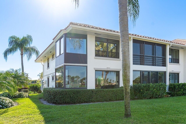 back of property featuring a tiled roof, a lawn, and stucco siding