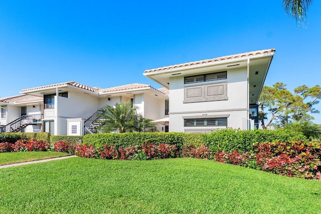 mediterranean / spanish home featuring a front lawn, a tile roof, and stucco siding