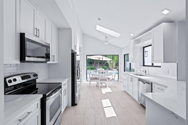 kitchen featuring stainless steel appliances, lofted ceiling with skylight, tasteful backsplash, and white cabinets