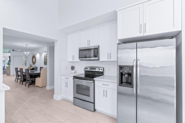 kitchen featuring pendant lighting, a chandelier, appliances with stainless steel finishes, and white cabinets