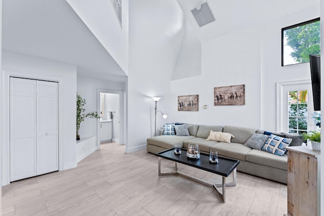 living area with visible vents, light wood-style flooring, a high ceiling, and baseboards