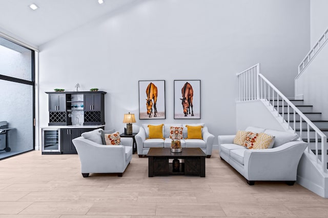 living area with wine cooler, stairs, light wood-style floors, and a towering ceiling