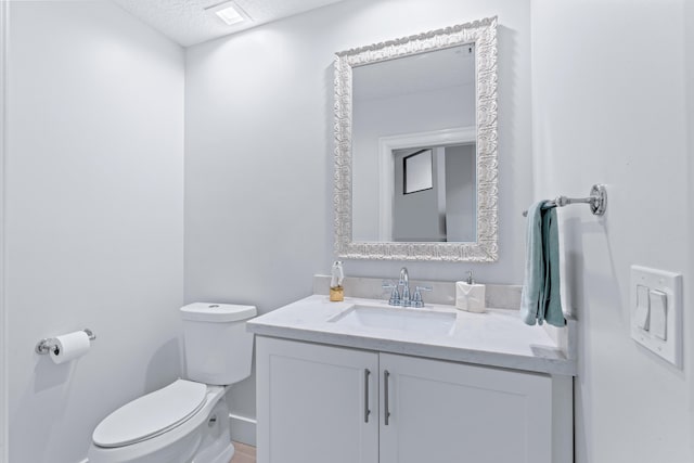 half bath featuring a textured ceiling, toilet, and vanity