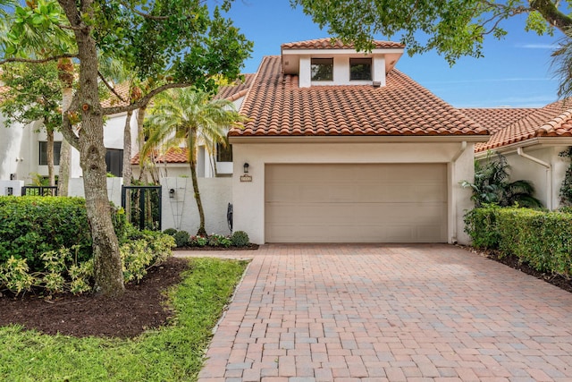 mediterranean / spanish home with stucco siding, a tiled roof, an attached garage, and decorative driveway