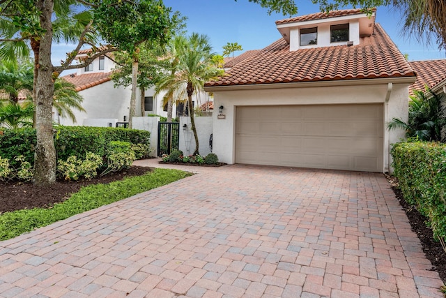 mediterranean / spanish-style house featuring a gate, an attached garage, stucco siding, a tiled roof, and decorative driveway