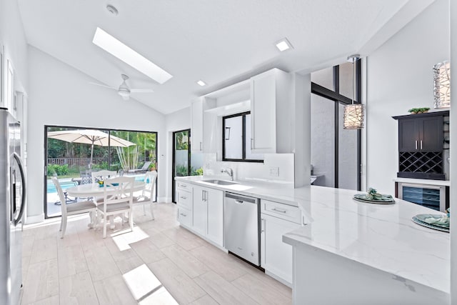 kitchen with light stone counters, a sink, white cabinetry, stainless steel appliances, and a skylight