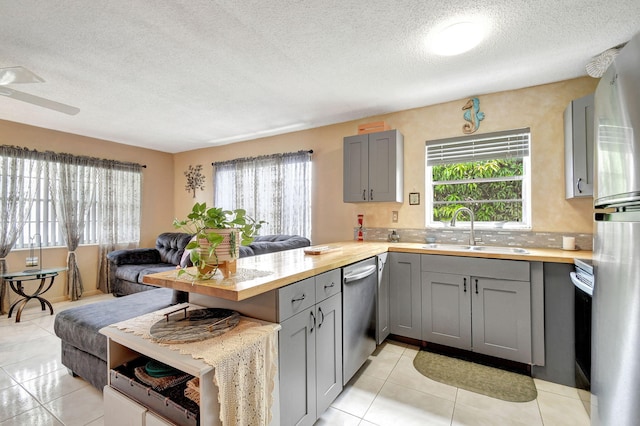 kitchen with gray cabinets, a sink, open floor plan, stainless steel appliances, and a peninsula