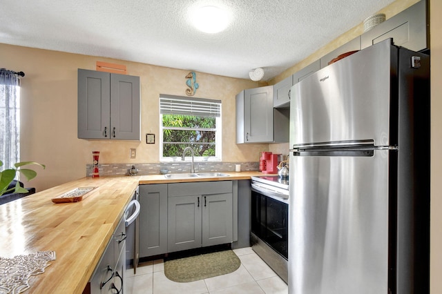 kitchen with butcher block countertops, gray cabinets, stainless steel appliances, and a sink