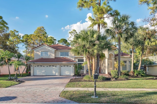 mediterranean / spanish house with decorative driveway, a front yard, a tile roof, and stucco siding