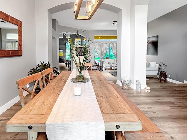 dining room featuring arched walkways, wood finished floors, and baseboards