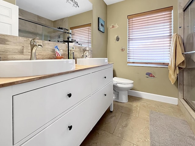 full bathroom with double vanity, a stall shower, baseboards, and a sink