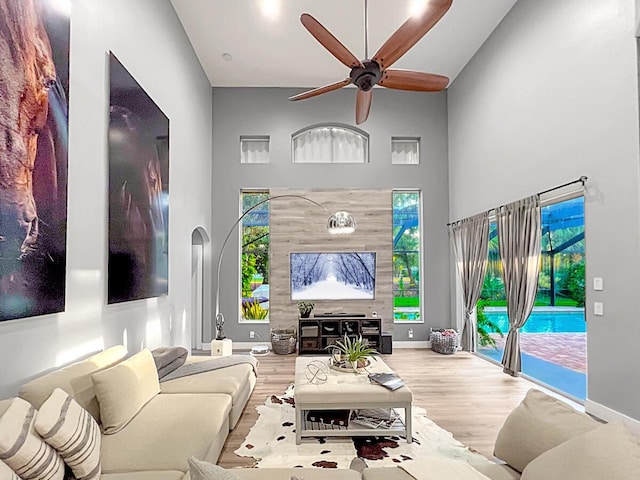 living area with arched walkways, a high ceiling, a ceiling fan, wood finished floors, and baseboards