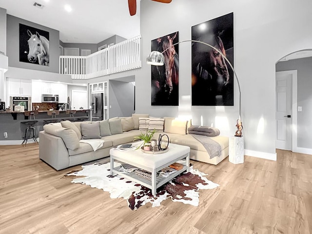 living room featuring light wood-type flooring, baseboards, a towering ceiling, and arched walkways