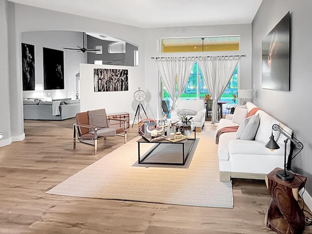 living room with ceiling fan, arched walkways, and wood finished floors