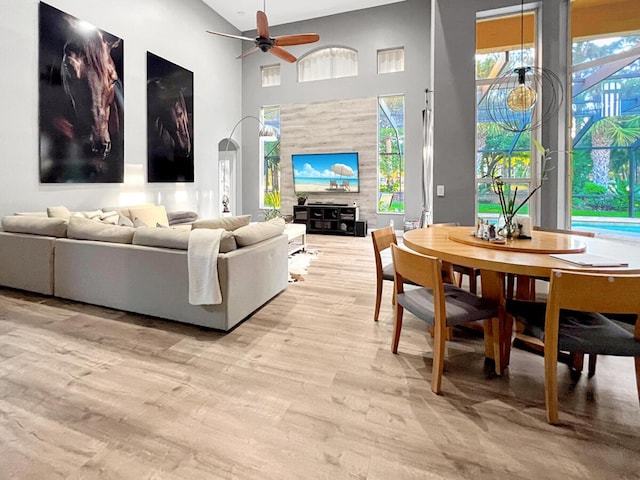 living area with arched walkways, a ceiling fan, a towering ceiling, and light wood-style floors