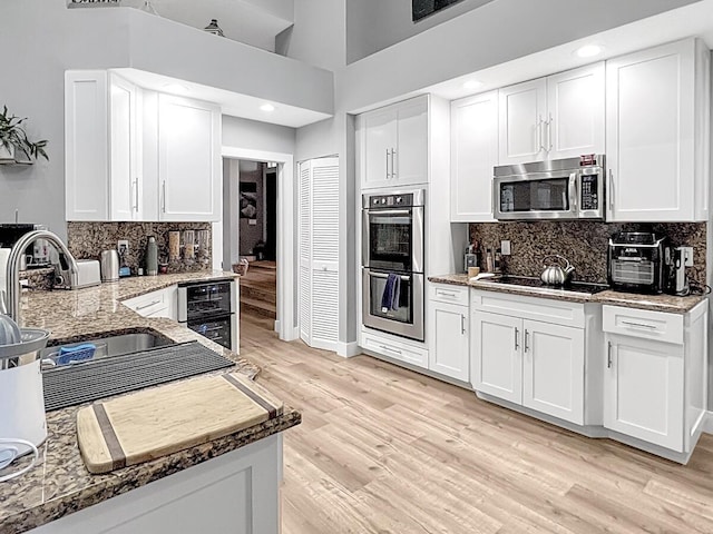 kitchen with white cabinets, wine cooler, appliances with stainless steel finishes, light wood-type flooring, and a sink