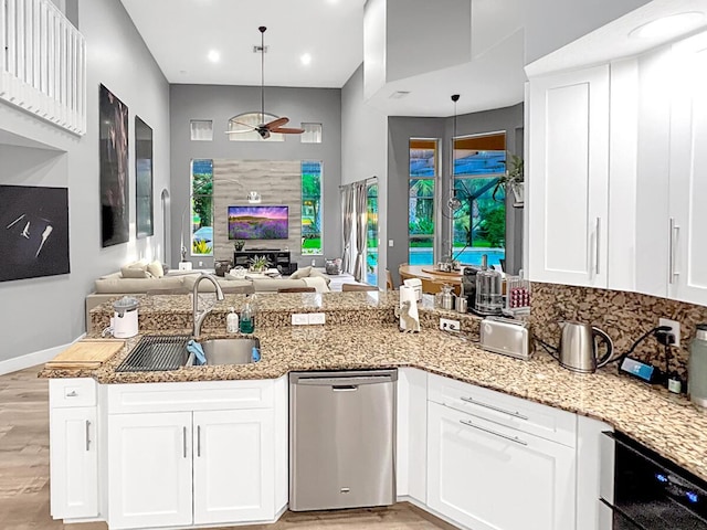 kitchen featuring dishwasher, light stone counters, open floor plan, light wood-style floors, and a sink