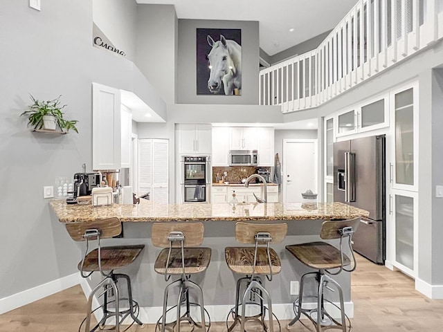 kitchen with a peninsula, appliances with stainless steel finishes, light stone counters, and light wood-style floors