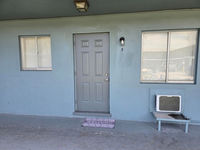 view of exterior entry with a wall unit AC and stucco siding