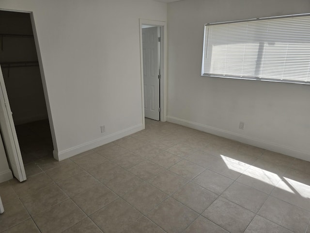 unfurnished bedroom with a spacious closet, tile patterned floors, and baseboards