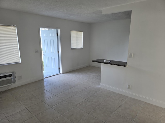 empty room with a textured ceiling, light tile patterned floors, a wall unit AC, and baseboards