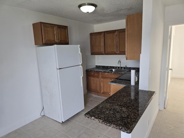 kitchen with light tile patterned flooring, dark stone countertops, a sink, and freestanding refrigerator